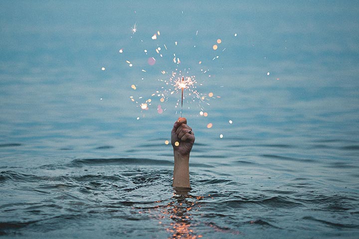 Hand emerging from the ocean holding a lit sparkler